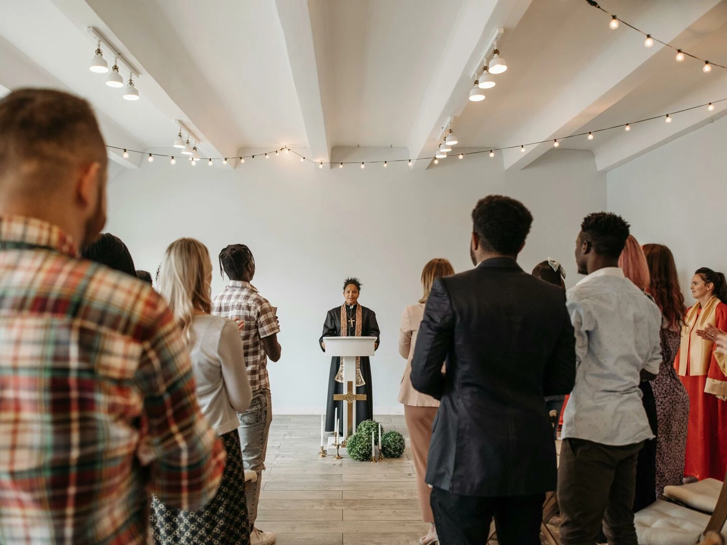 a diverse congregation stands together in prayer led by a woman pastor indoors