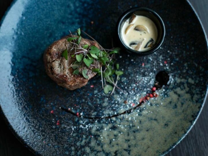 Elegant plated steak dish garnished with microgreens and served with creamy mushroom sauce.