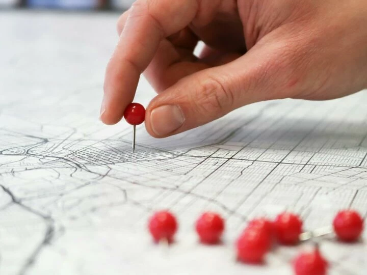 Close-up of a hand placing a red pin on a map indicating geographic location pinning.