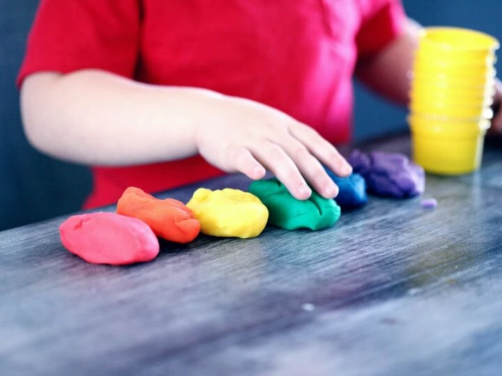 A young child with rainbow-colored modeling clay and stacking cups on a table indoors.