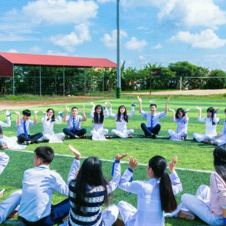 People Sitting on Green Lawn Grass While Doing Hands Up at Daytime