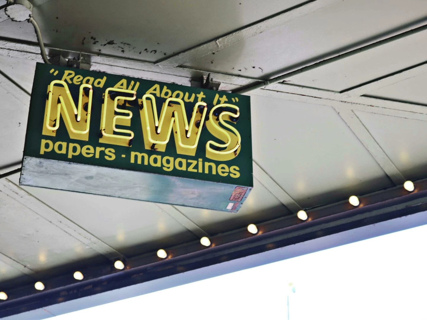 from below of illuminated signboard with news papers magazines inscriptions hanging on metal ceiling on street