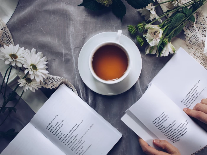 white ceramic teacup with saucer near two books above gray floral textile