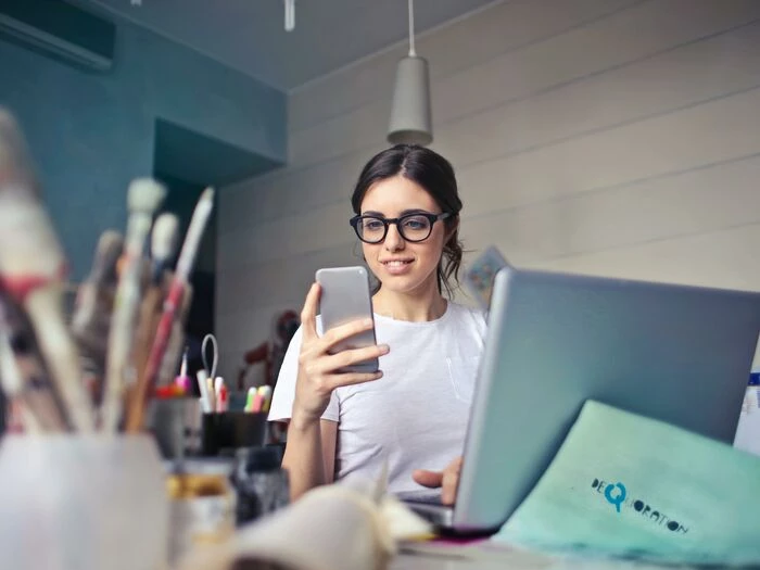 woman in white tshirt holding smartphone in front of laptop
